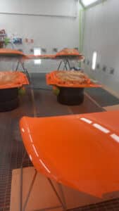 Cabine de peinture automobile. Pièces de carrosserie orange vif fraîchement peintes, dont un capot brillant en premier plan. Équipement ANEST IWATA.