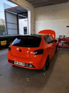 Seat Ibiza orange tuning dans garage, capot ouvert. Toit noir, vitres teintées, texte ZOUT GANG, sticker FAKE TAXI. Plaque FR BM-384-ZM.